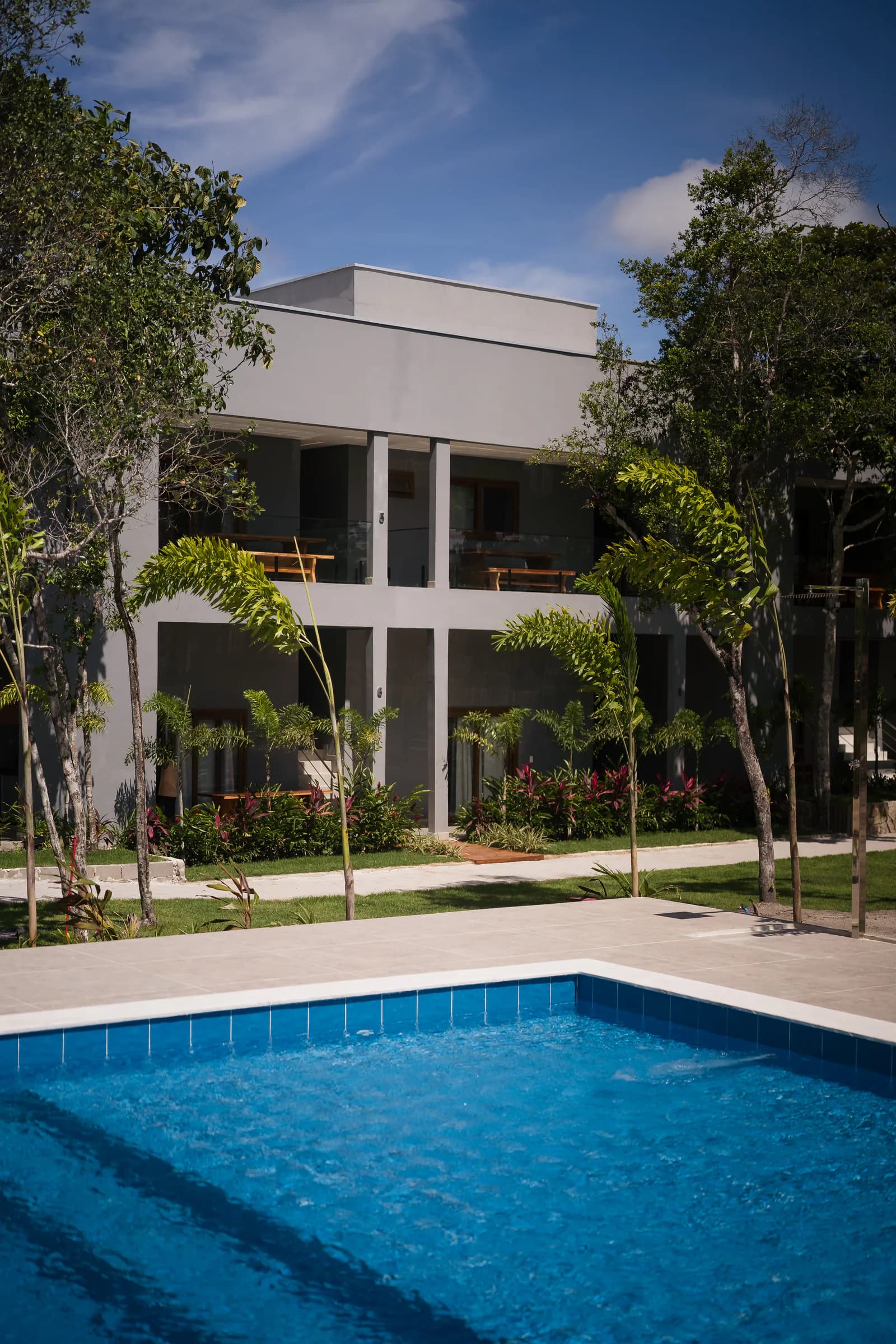 Piscina diante da fachada e das árvores no Residencial Marinho, Arraial d’Ajuda.